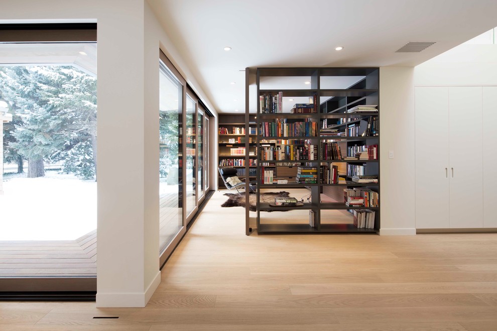Bild på ett stort funkis arbetsrum, med ett bibliotek, vita väggar, ljust trägolv, brunt golv och ett fristående skrivbord