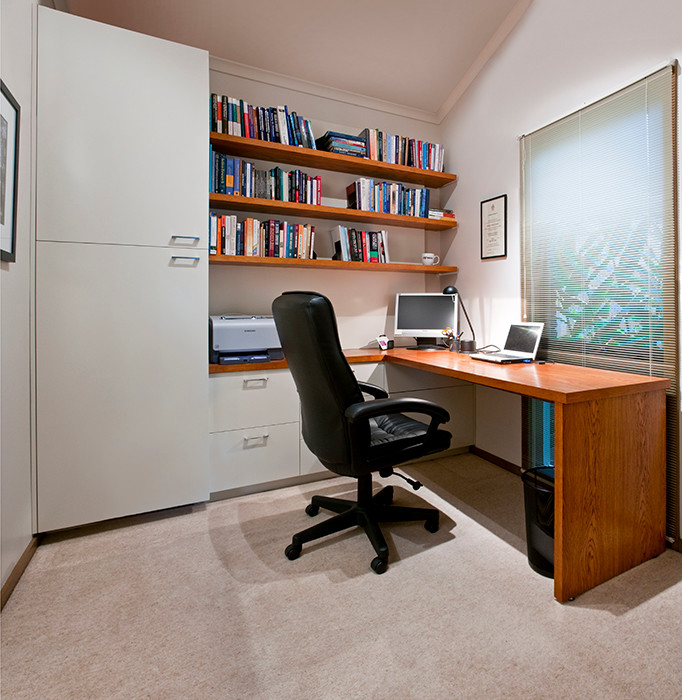 Modern inredning av ett mellanstort arbetsrum, med vita väggar, heltäckningsmatta och ett inbyggt skrivbord