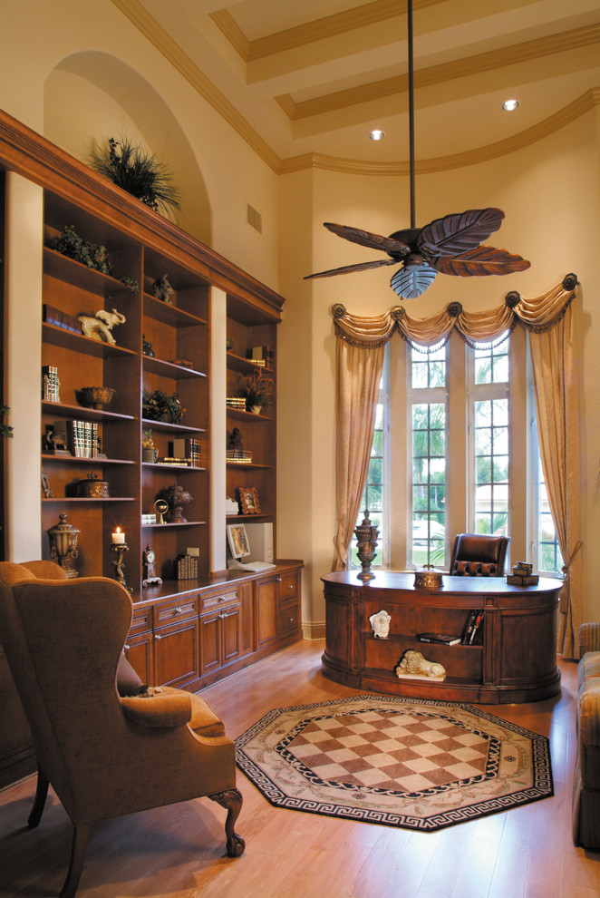 Modelo de despacho tradicional grande sin chimenea con paredes beige, suelo de madera en tonos medios y escritorio independiente