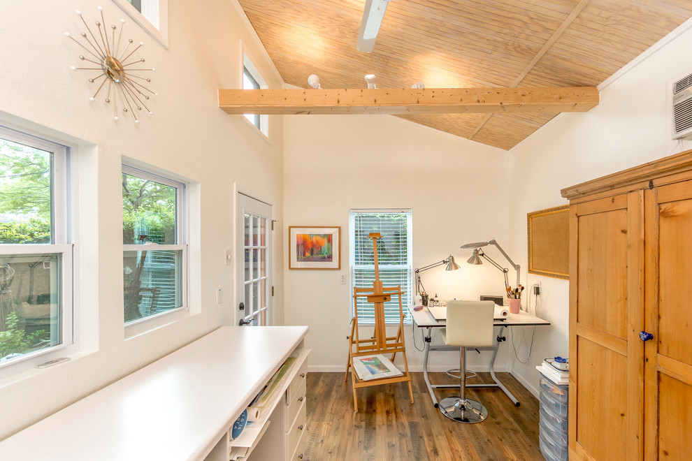 Skandinavisk inredning av ett litet hemmastudio, med vita väggar, laminatgolv, en öppen hörnspis, ett inbyggt skrivbord och brunt golv