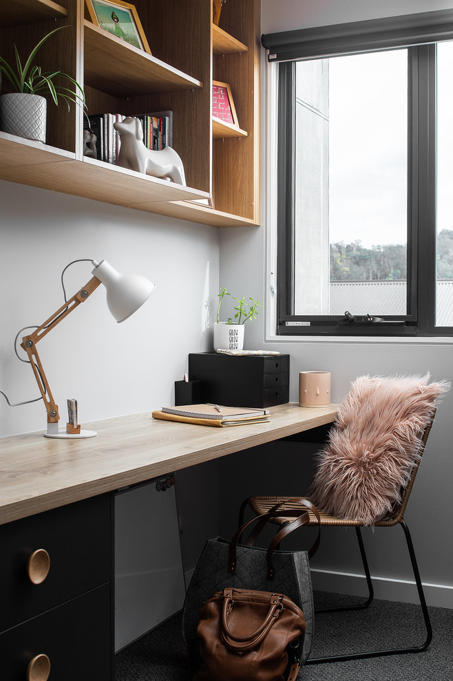 На фото: кабинет в скандинавском стиле с белыми стенами, ковровым покрытием, встроенным рабочим столом и серым полом