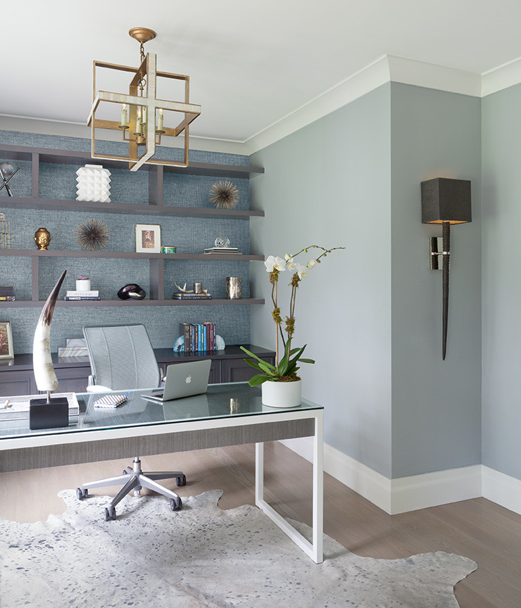 Modelo de despacho contemporáneo de tamaño medio sin chimenea con paredes azules, suelo de madera clara y escritorio independiente