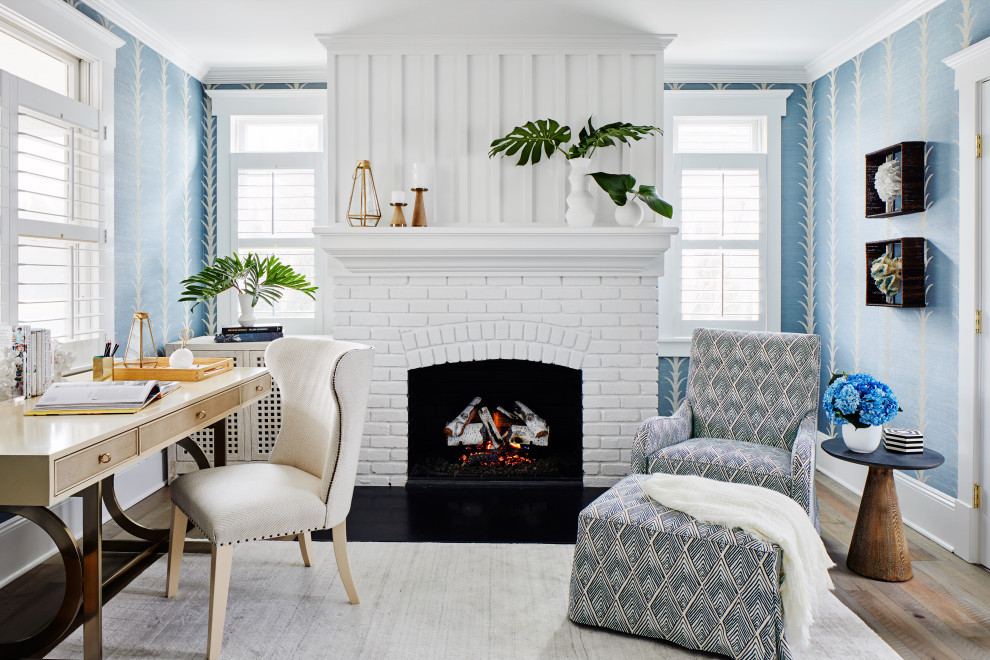 ニューヨークにある高級な中くらいなビーチスタイルのおしゃれなホームオフィス・書斎 (青い壁、標準型暖炉、レンガの暖炉まわり、自立型机、茶色い床、壁紙、淡色無垢フローリング) の写真