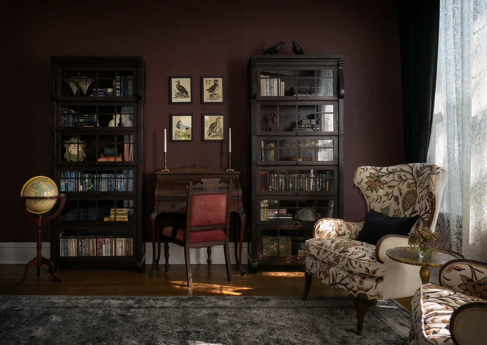 Modelo de despacho tradicional con biblioteca, suelo de madera en tonos medios, estufa de leña, marco de chimenea de ladrillo, escritorio independiente y suelo marrón