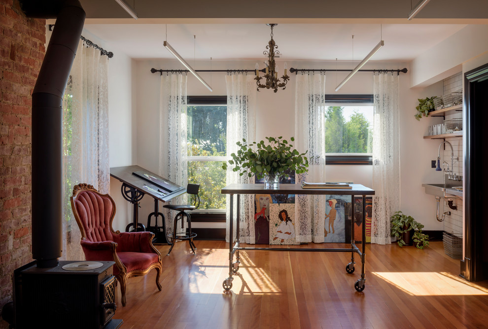 Klassisches Arbeitszimmer mit Studio, weißer Wandfarbe, braunem Holzboden, Kaminofen, Kaminumrandung aus Backstein, freistehendem Schreibtisch und braunem Boden in Seattle