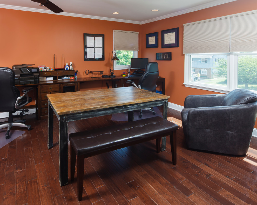 Foto på ett stort funkis hemmabibliotek, med orange väggar, mörkt trägolv och ett fristående skrivbord