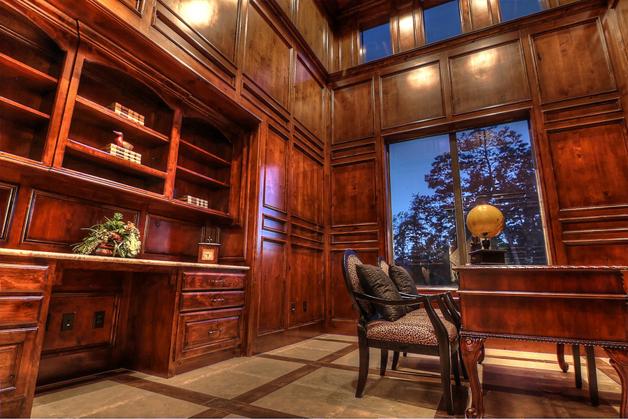 Foto på ett stort medelhavsstil hemmabibliotek, med bruna väggar, kalkstensgolv och ett fristående skrivbord