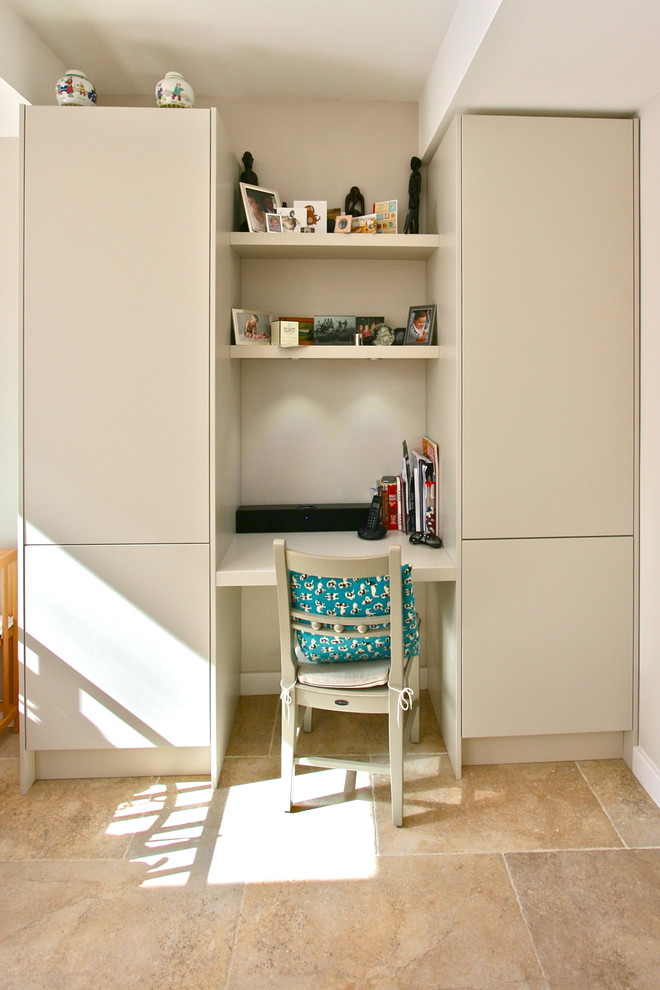 Medium sized contemporary study in London with beige walls, travertine flooring, no fireplace and a built-in desk.