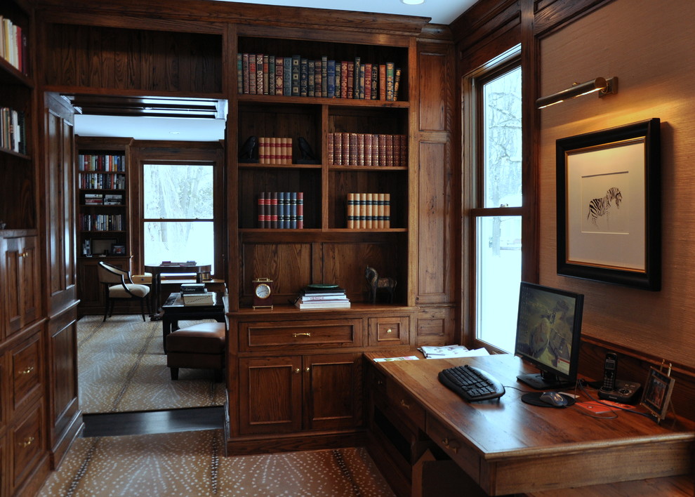 Bild på ett mellanstort amerikanskt hemmabibliotek, med mörkt trägolv, ett inbyggt skrivbord och beige väggar