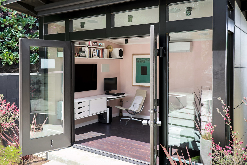This is an example of a small modern home studio in Los Angeles with pink walls, vinyl flooring, no fireplace, a built-in desk and brown floors.