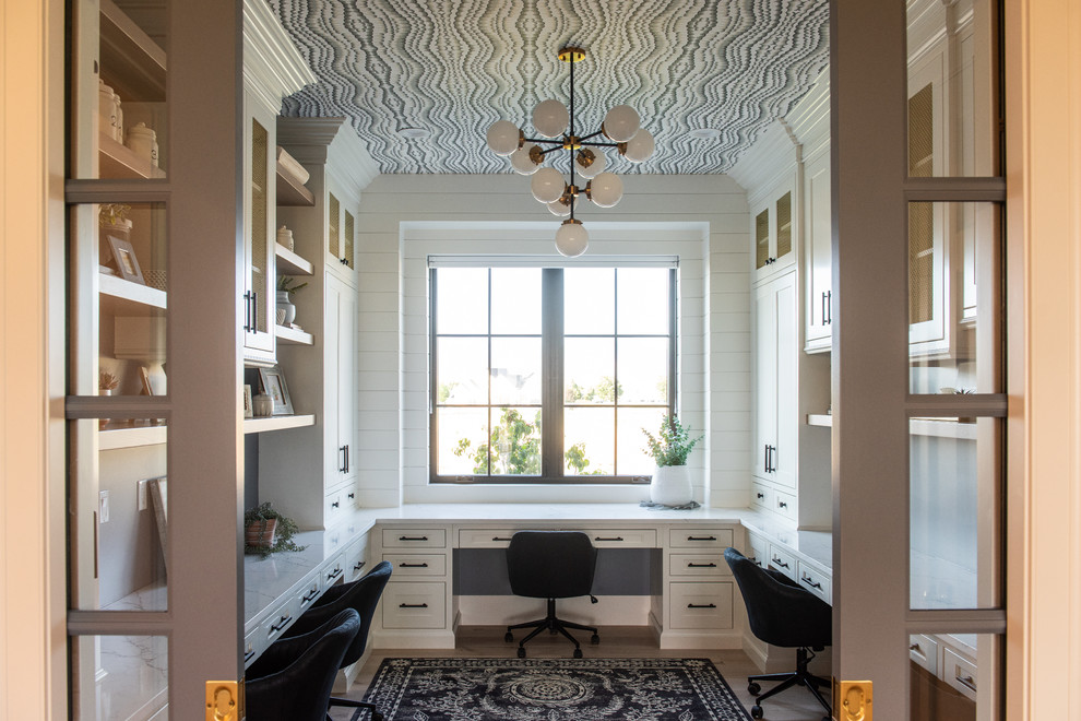 Modelo de despacho tradicional renovado con paredes blancas, suelo de madera clara, escritorio empotrado y suelo beige