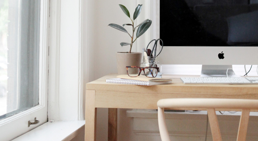 Minimalistisk inredning av ett mellanstort hemmastudio, med vita väggar, ljust trägolv och ett fristående skrivbord