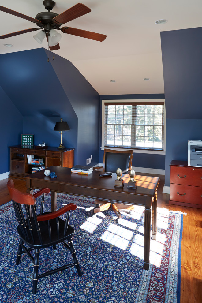 Bild på ett hemmabibliotek, med blå väggar, mellanmörkt trägolv och ett fristående skrivbord