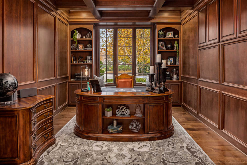 Modelo de despacho tradicional de tamaño medio sin chimenea con paredes marrones, suelo de madera en tonos medios, escritorio independiente y suelo marrón