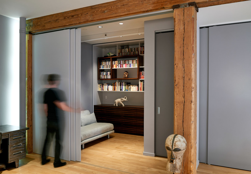 Foto de despacho industrial con biblioteca, paredes grises y suelo de madera clara