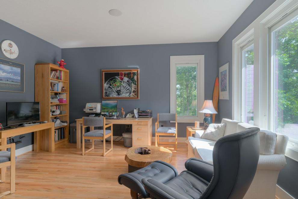 Modern inredning av ett mellanstort arbetsrum, med grå väggar, ljust trägolv och ett fristående skrivbord