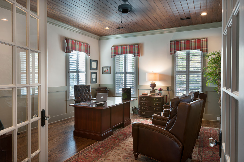 Großes Klassisches Arbeitszimmer mit grauer Wandfarbe, braunem Holzboden, freistehendem Schreibtisch, braunem Boden, Holzdecke und vertäfelten Wänden in Sonstige