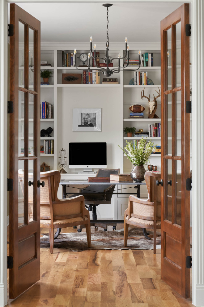 Cette image montre un bureau rustique de taille moyenne avec une bibliothèque ou un coin lecture, un mur blanc, un sol en bois brun, un bureau indépendant et un sol marron.