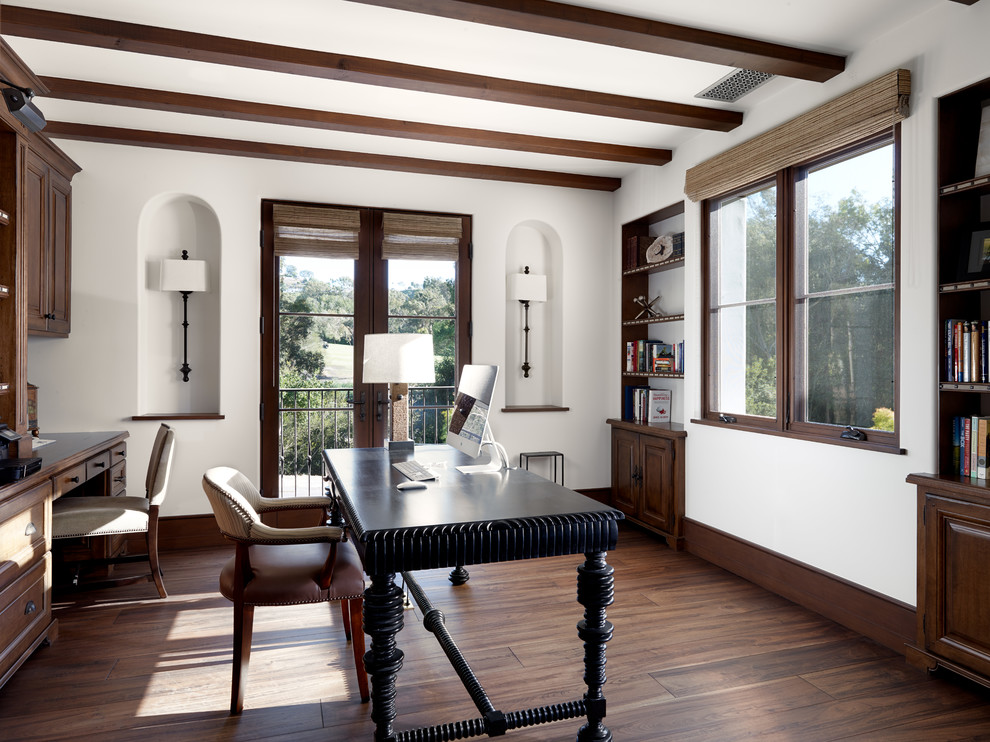 Home office - mediterranean freestanding desk dark wood floor home office idea in Los Angeles with white walls