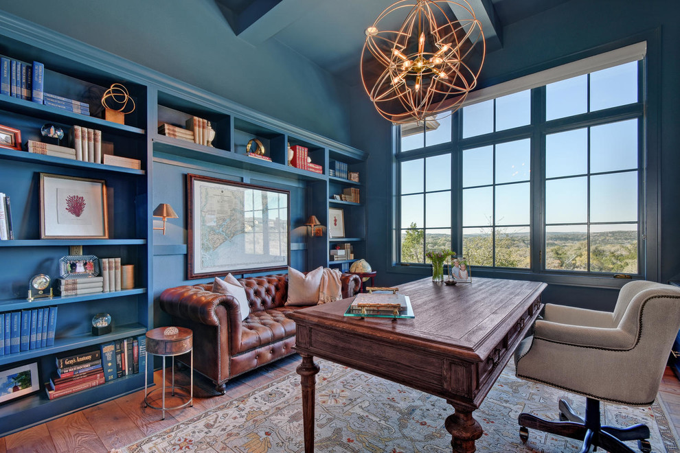 Großes Klassisches Arbeitszimmer ohne Kamin mit Arbeitsplatz, blauer Wandfarbe, freistehendem Schreibtisch und braunem Holzboden in Austin
