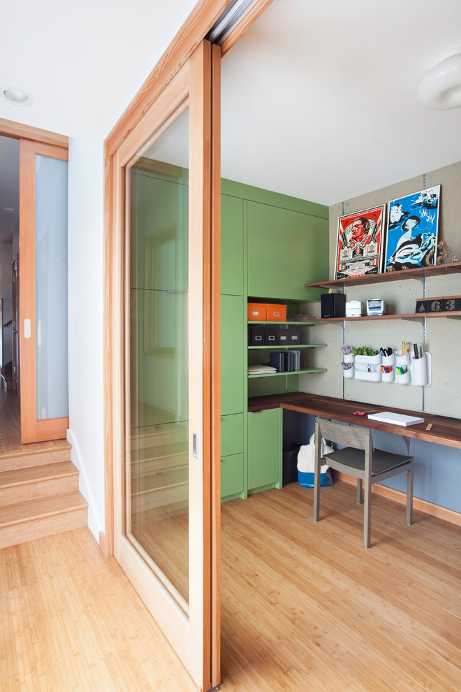 Cette photo montre un petit bureau tendance avec un mur vert, un sol en bois brun et un bureau intégré.