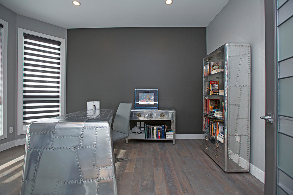Bild på ett mellanstort funkis hemmabibliotek, med grå väggar, mellanmörkt trägolv, ett fristående skrivbord och grått golv