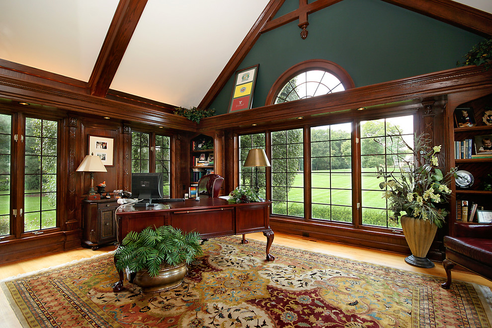 Klassisk inredning av ett stort hemmabibliotek, med gröna väggar, ljust trägolv och ett fristående skrivbord