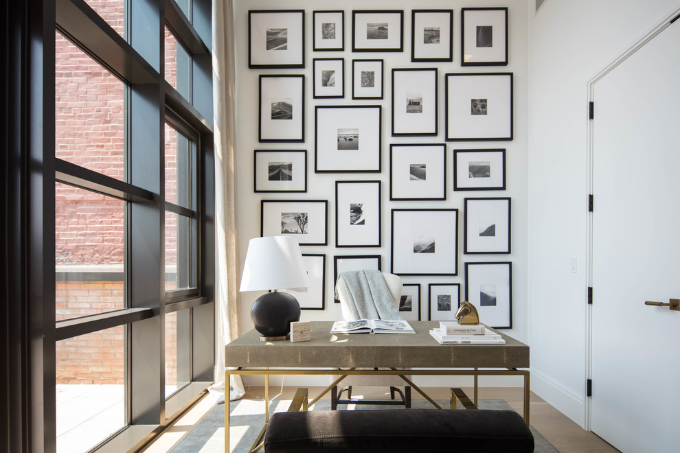 Diseño de despacho contemporáneo sin chimenea con paredes blancas, suelo de madera clara y escritorio independiente