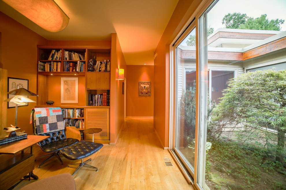 Foto de despacho actual pequeño con parades naranjas, suelo de madera clara y escritorio empotrado
