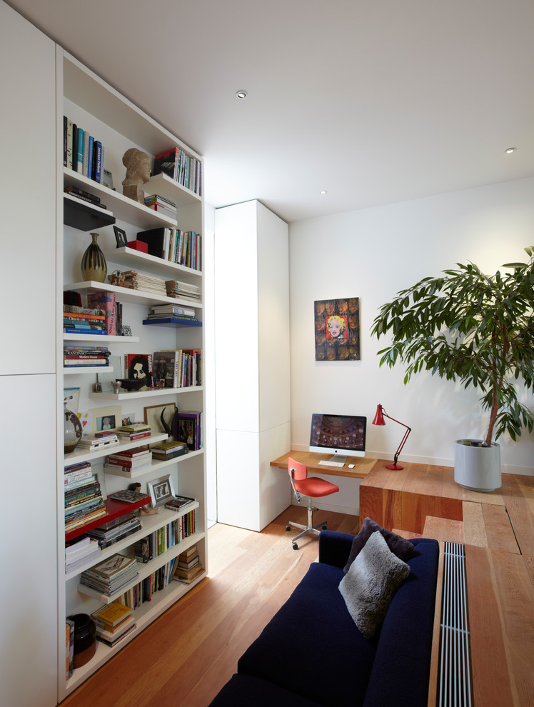 Inspiration för mellanstora moderna arbetsrum, med vita väggar, ett bibliotek, mellanmörkt trägolv, ett inbyggt skrivbord och brunt golv