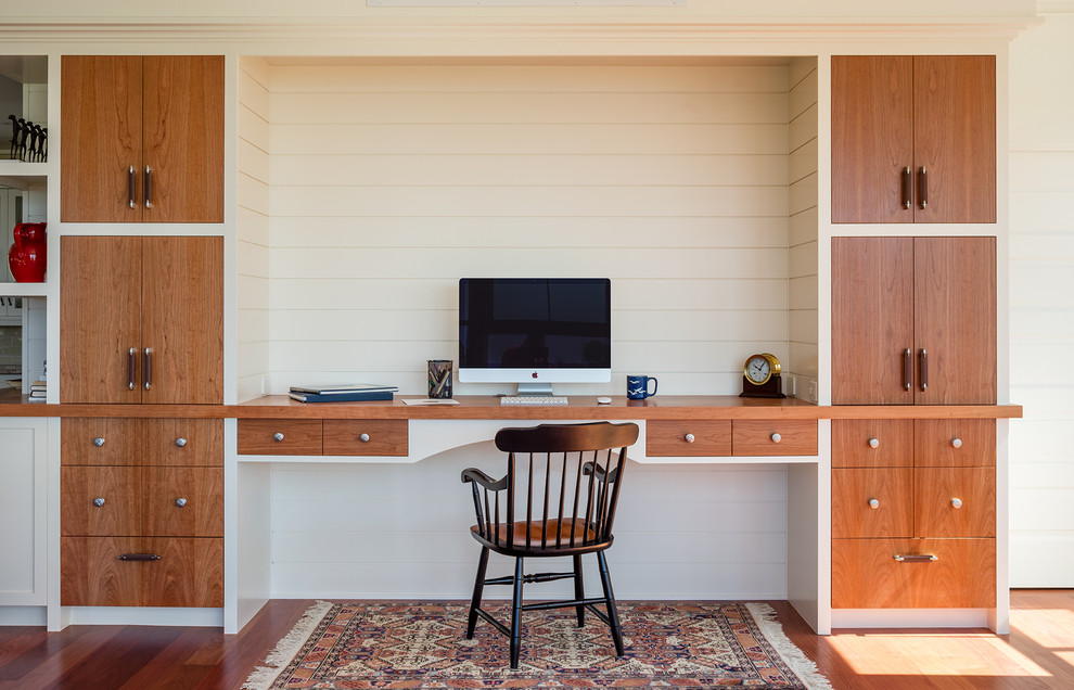 На фото: кабинет в морском стиле с белыми стенами, темным паркетным полом, встроенным рабочим столом и коричневым полом с