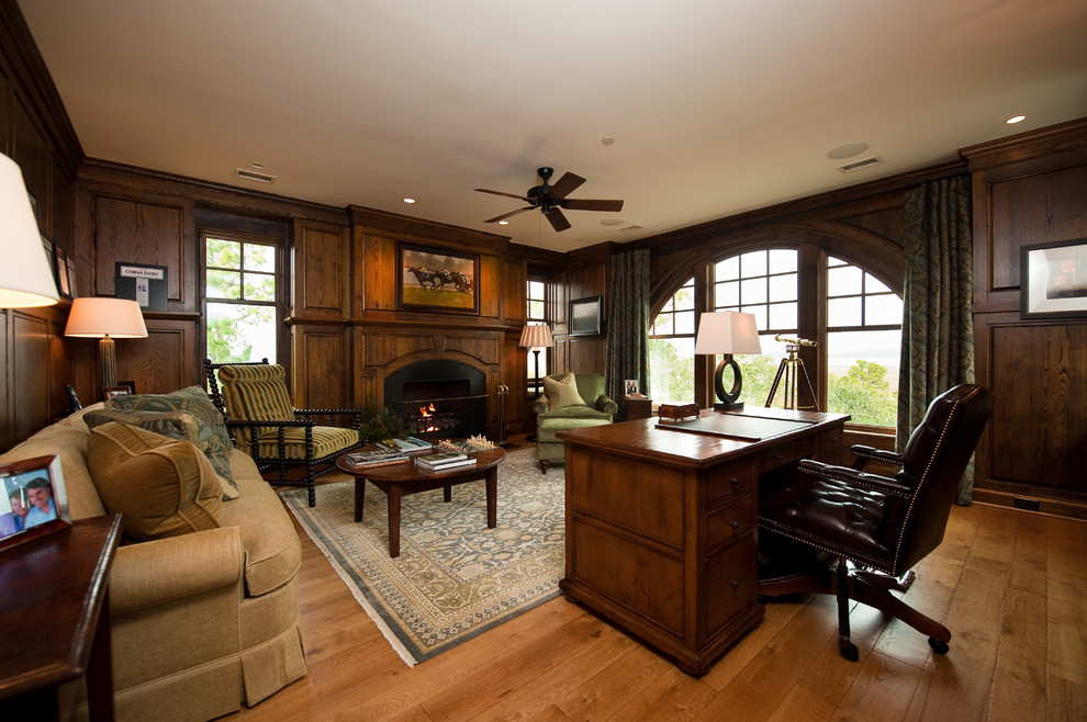 Mittelgroßes Klassisches Arbeitszimmer mit Arbeitsplatz, brauner Wandfarbe, braunem Holzboden, Kamin und freistehendem Schreibtisch in Charleston