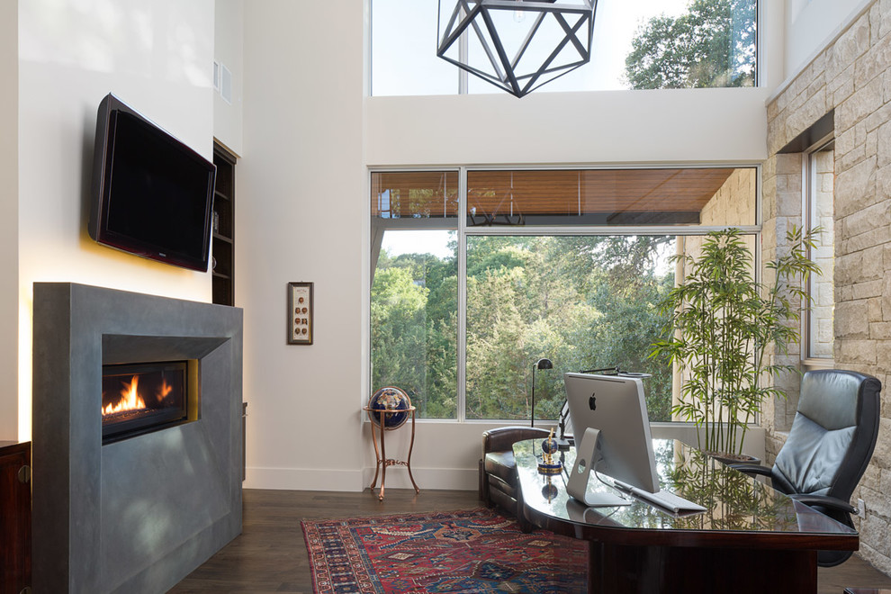 オースティンにある高級な中くらいなコンテンポラリースタイルのおしゃれな書斎 (白い壁、濃色無垢フローリング、横長型暖炉、自立型机、コンクリートの暖炉まわり) の写真