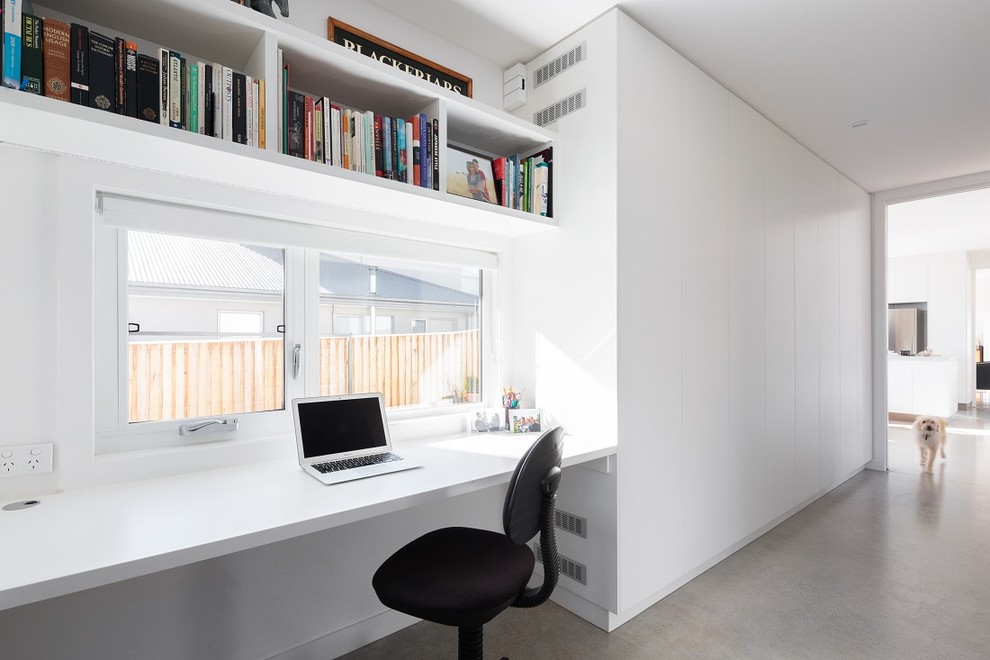 На фото: кабинет в стиле модернизм с белыми стенами, бетонным полом и встроенным рабочим столом