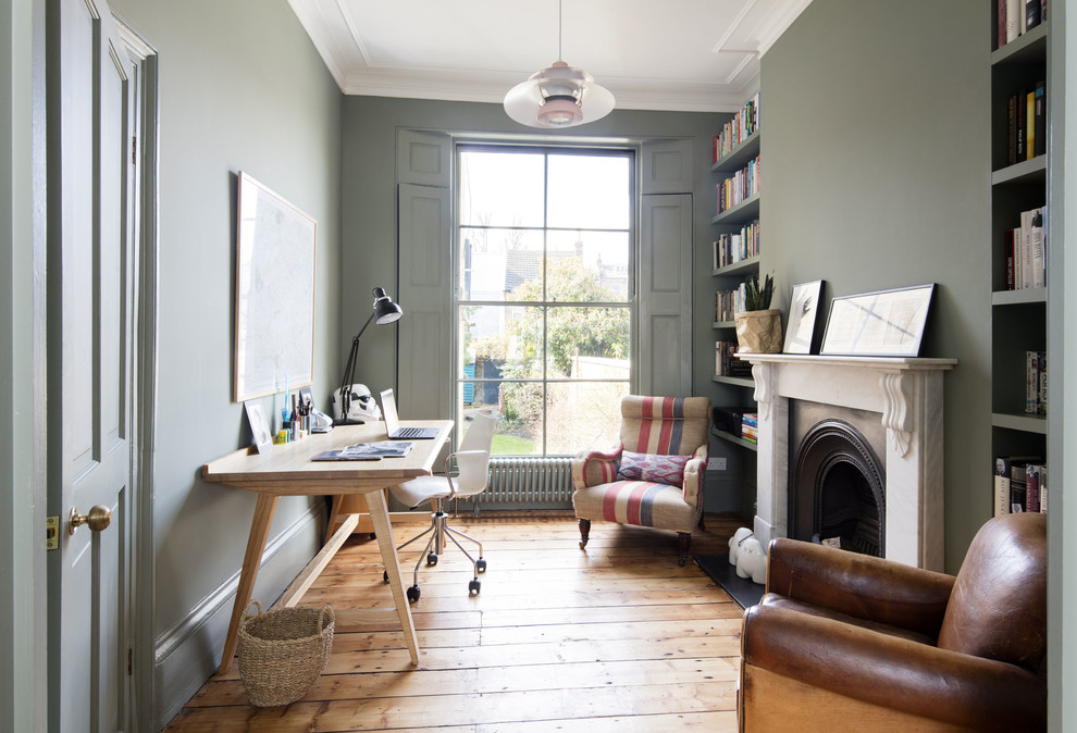 ロンドンにあるトランジショナルスタイルのおしゃれな書斎 (緑の壁、無垢フローリング、自立型机、茶色い床、標準型暖炉) の写真