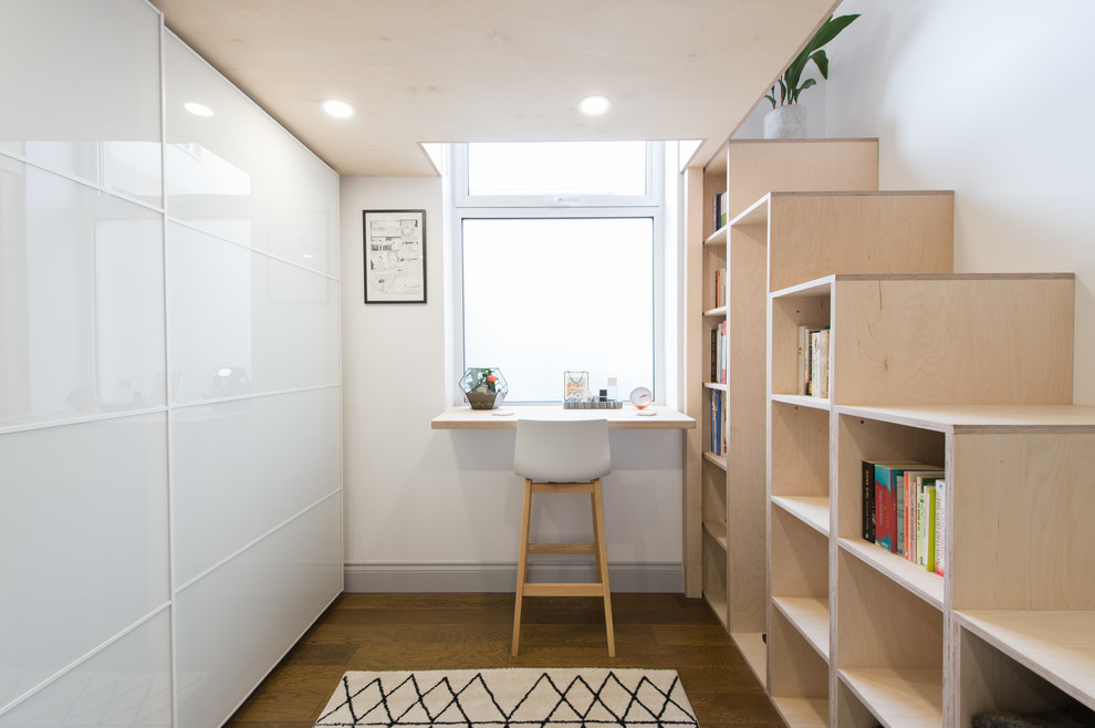 Foto på ett minimalistiskt arbetsrum, med ett bibliotek, vita väggar, mörkt trägolv, ett inbyggt skrivbord och brunt golv