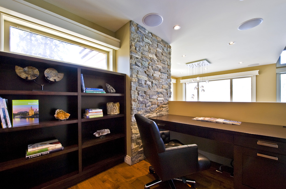 Ejemplo de despacho actual con paredes amarillas, suelo de madera oscura y escritorio empotrado