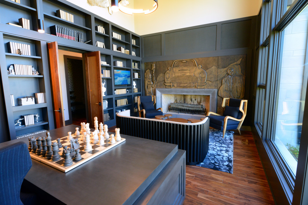 Großes Modernes Arbeitszimmer mit Arbeitsplatz, grauer Wandfarbe, braunem Holzboden, Kamin, Kaminumrandung aus Beton, freistehendem Schreibtisch und braunem Boden in Indianapolis
