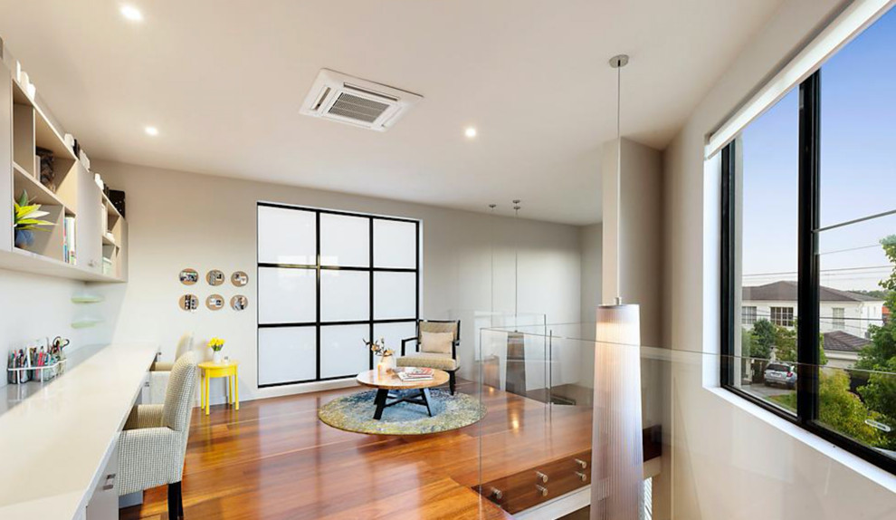 Modernes Arbeitszimmer mit grauer Wandfarbe, braunem Holzboden und Einbau-Schreibtisch in Melbourne