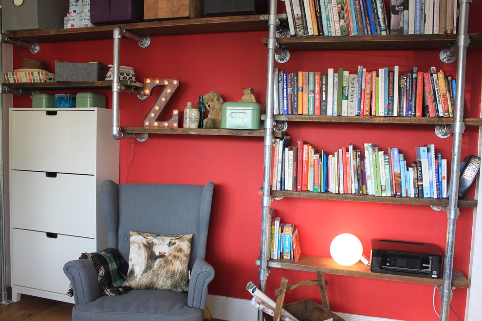 Foto på ett mellanstort funkis hemmabibliotek, med röda väggar och mellanmörkt trägolv