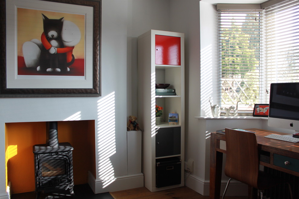Imagen de despacho contemporáneo de tamaño medio con paredes blancas, suelo de madera en tonos medios, estufa de leña y escritorio independiente