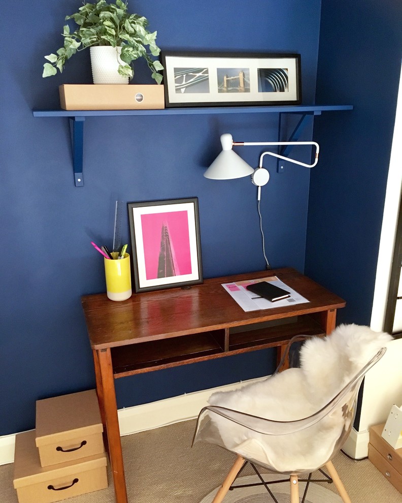 Modern inredning av ett litet hemmabibliotek, med blå väggar, heltäckningsmatta och ett fristående skrivbord