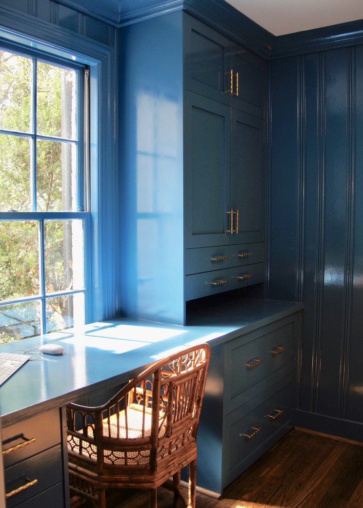 Cette image montre un petit bureau craftsman avec un mur bleu, parquet foncé, un bureau intégré et un sol marron.