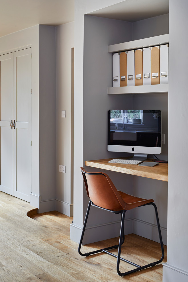 Diseño de despacho clásico renovado pequeño sin chimenea con paredes grises, suelo de madera clara y escritorio empotrado