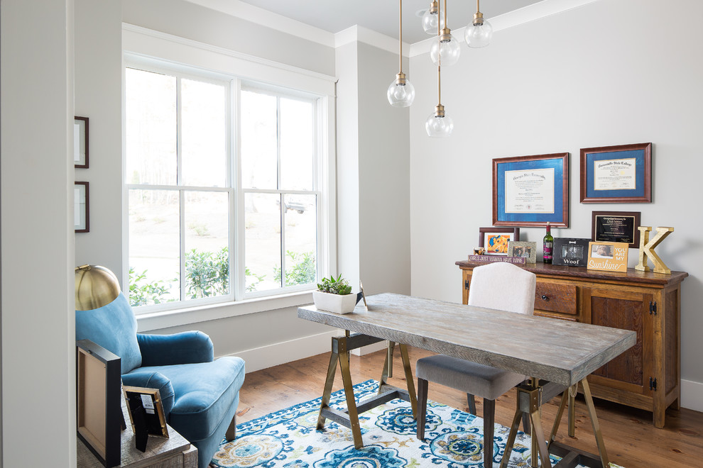 Landhaus Arbeitszimmer mit grauer Wandfarbe, braunem Holzboden, freistehendem Schreibtisch und braunem Boden in Atlanta