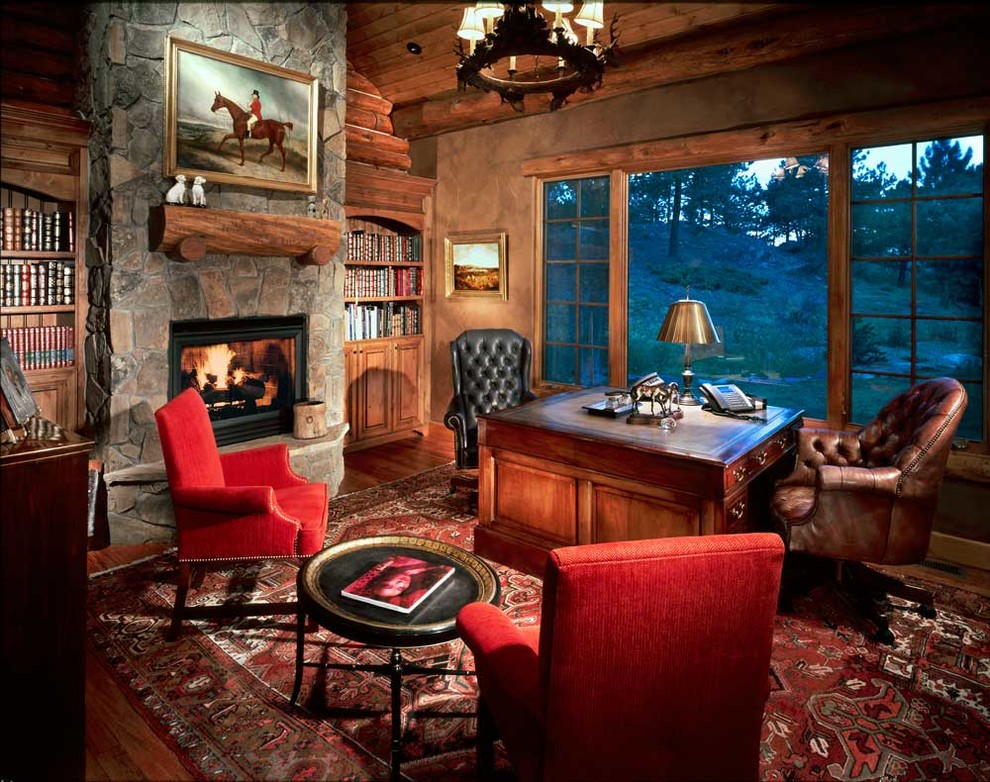 Exempel på ett mellanstort klassiskt hemmabibliotek, med bruna väggar, mellanmörkt trägolv, en standard öppen spis, en spiselkrans i sten och ett fristående skrivbord