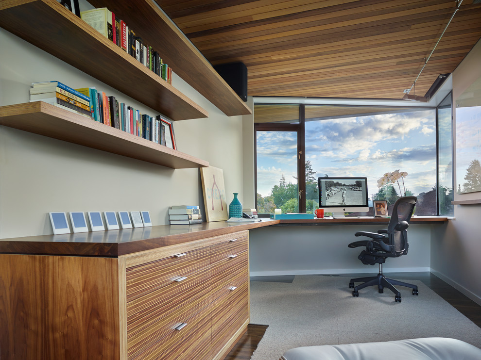 Bild på ett funkis arbetsrum, med grå väggar, mörkt trägolv och ett inbyggt skrivbord