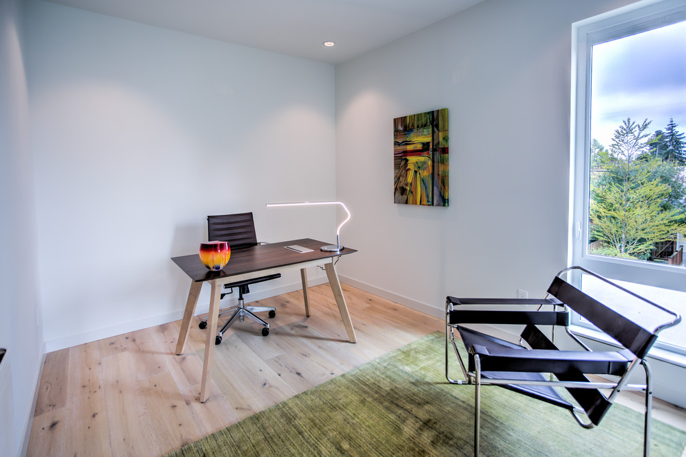 Modern inredning av ett mellanstort arbetsrum, med vita väggar, ljust trägolv och ett fristående skrivbord