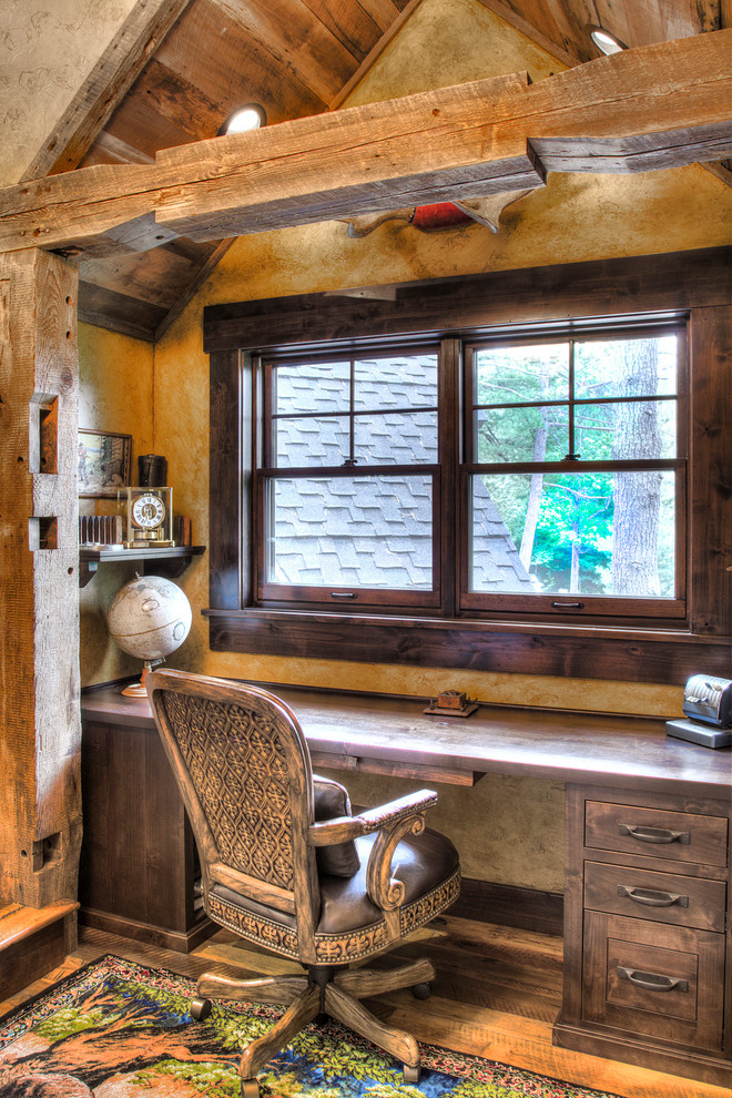 Photo of a small rustic study in Minneapolis with yellow walls, medium hardwood flooring, a built-in desk and beige floors.