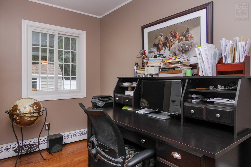 Mittelgroßes Arbeitszimmer ohne Kamin mit beiger Wandfarbe, braunem Holzboden und freistehendem Schreibtisch in New York